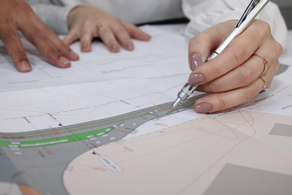Mãos de profissionais engenheiros analisando a regularização de um acesso rodoviário em uma rodovia federal para aprovação no DNIT.